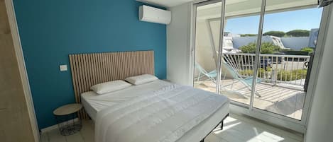 A bedroom with a bed, a bedside table, a chair, and a view of the outside.