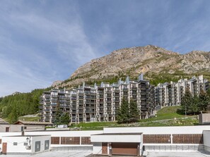 A multi-story hotel with balconies, set against a mountainous backdrop. - Charming apartment with wifi - 4 guests (Val-d'Isère)