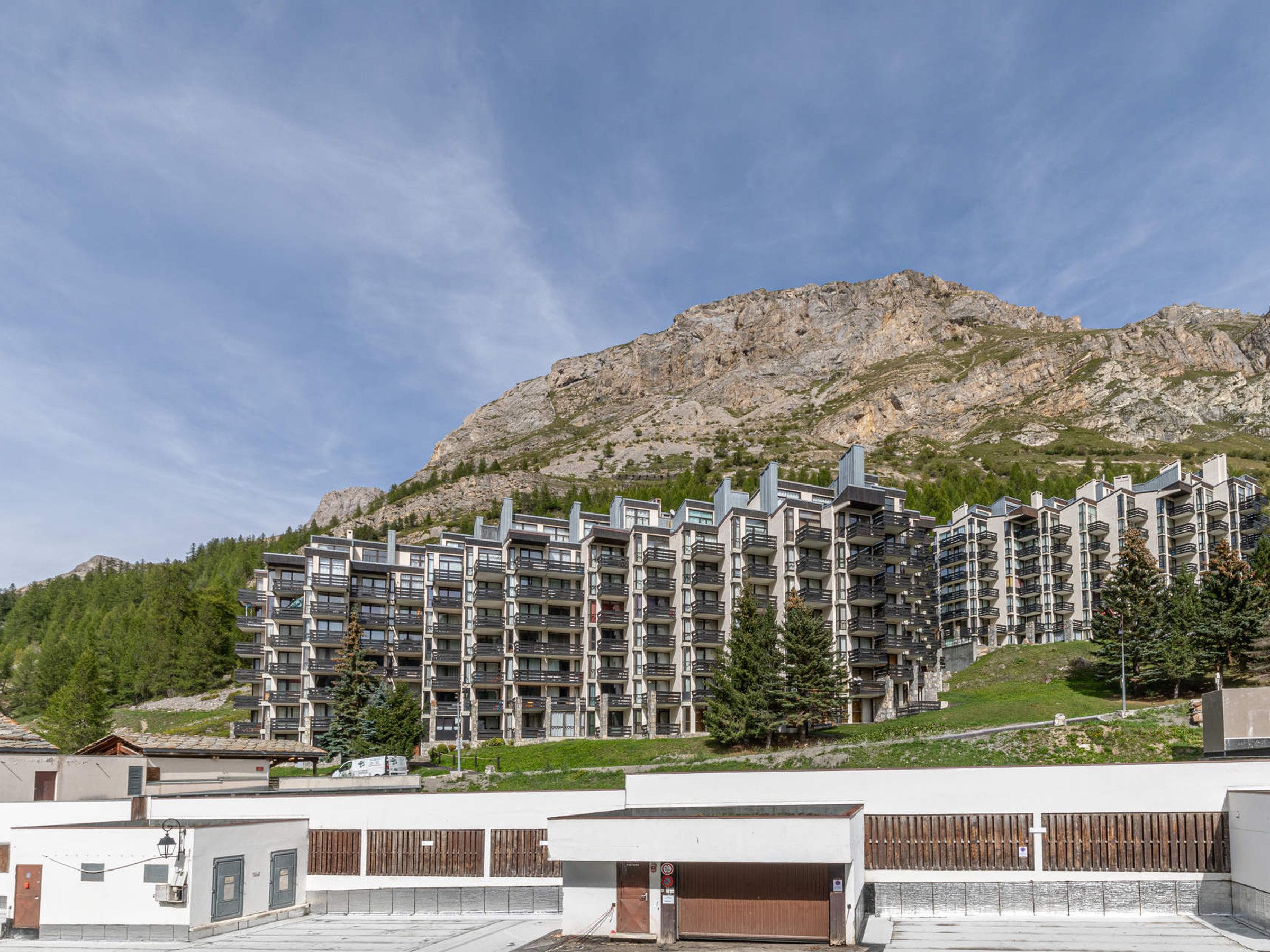 A multi-story hotel with balconies, set against a mountainous backdrop.