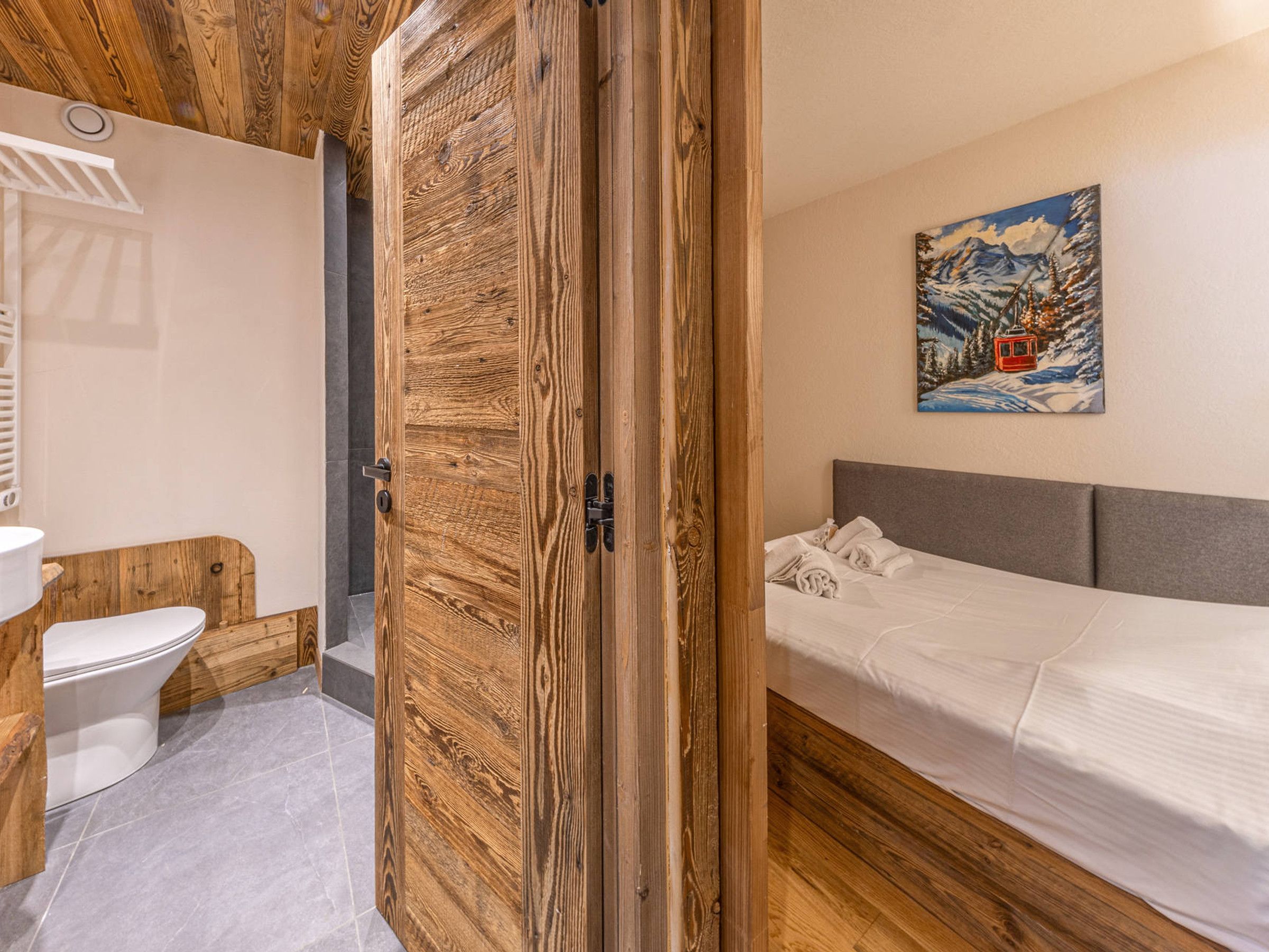 Une chambre avec une porte en bois, un lit, un tableau et une salle de bain avec des toilettes.