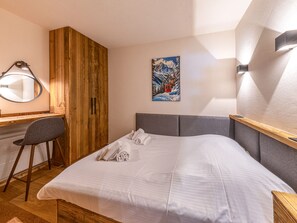 A hotel room with a bed, a desk, a chair, a wooden wardrobe, a painting, and a wall-mounted light fixture. - Charming apartment with wifi - 4 guests (Val-d'Isère)