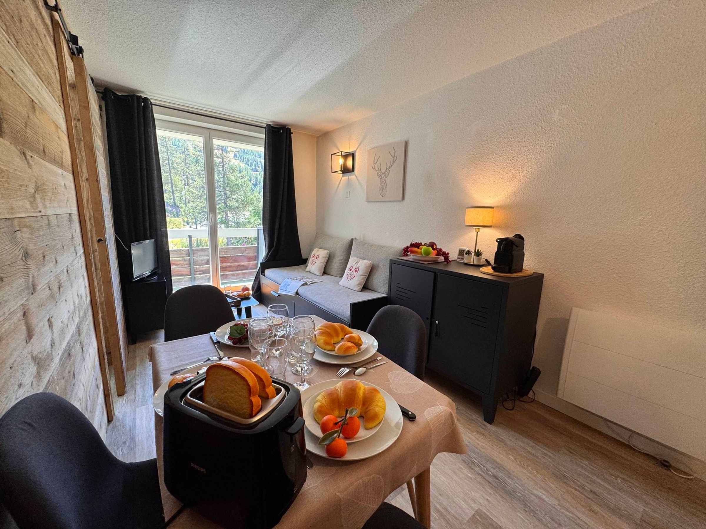 A cozy room with a dining table set for two, a sofa, a cabinet, and a TV.