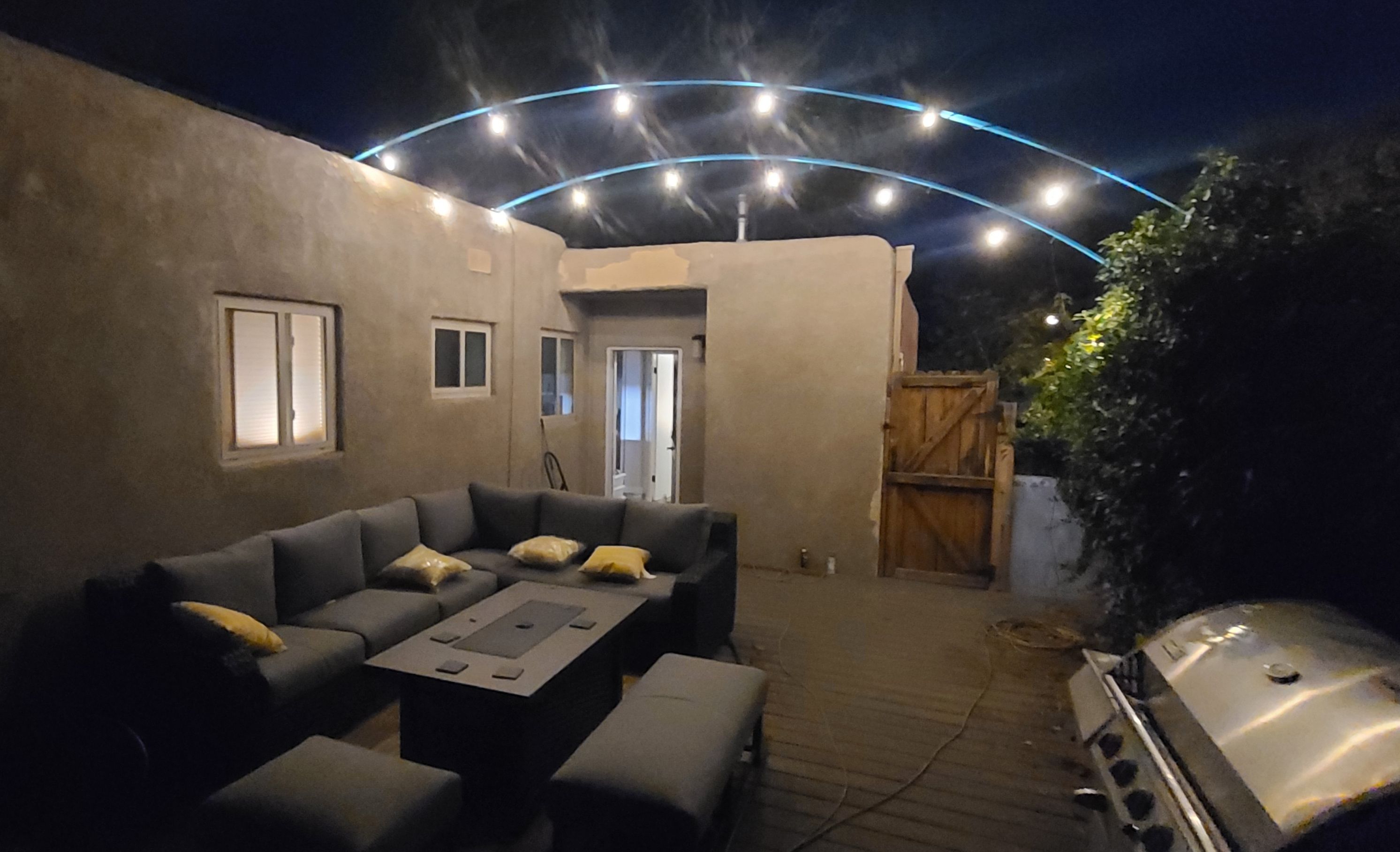 An outdoor patio area with a sofa set, a grill, and a curved light installation.
