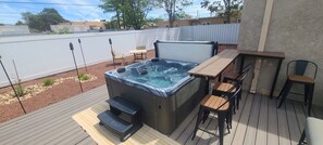 Ein Whirlpool auf einer Holzdiele mit Tisch und Stühlen, umgeben von einem Zaun und Blick auf eine Wohngegend.