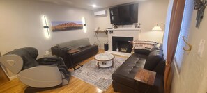 Ein Wohnzimmer mit Sofa, Sessel, Fernseher, Kamin und einem an der Wand hängenden Kunstwerk.