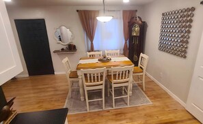 Un coin repas avec une table en bois, des chaises blanches, un miroir décoratif, une horloge murale et un mur entièrement recouvert de miroirs.