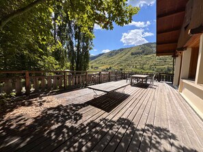 A wooden deck with a table and chairs, overlooking a hilly landscape.
