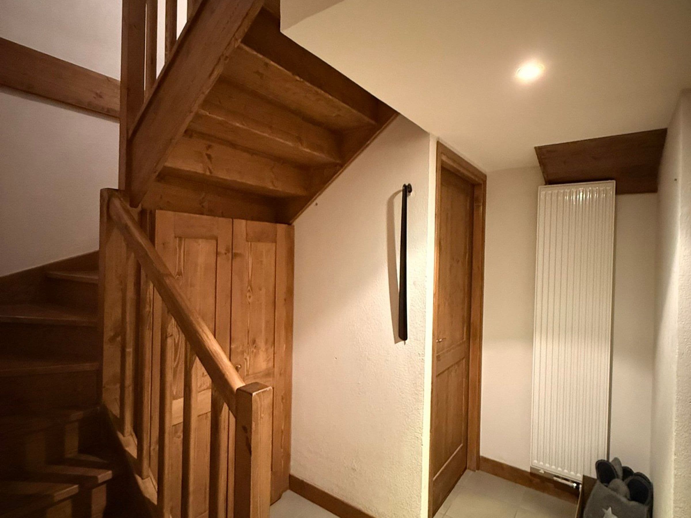A wooden staircase leading to a room with a door and a radiator.