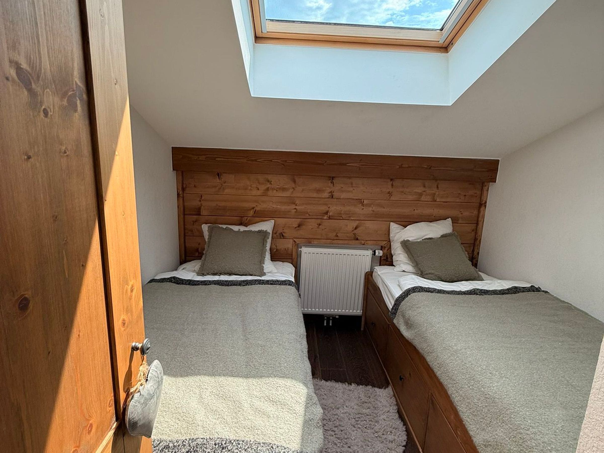A bedroom with two beds, a skylight, and a radiator.