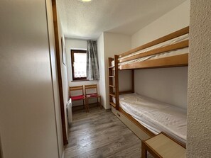 Ein kleines Zimmer mit Etagenbett, einem Schreibtisch mit Stuhl und einem fenster mit Vorhängen.