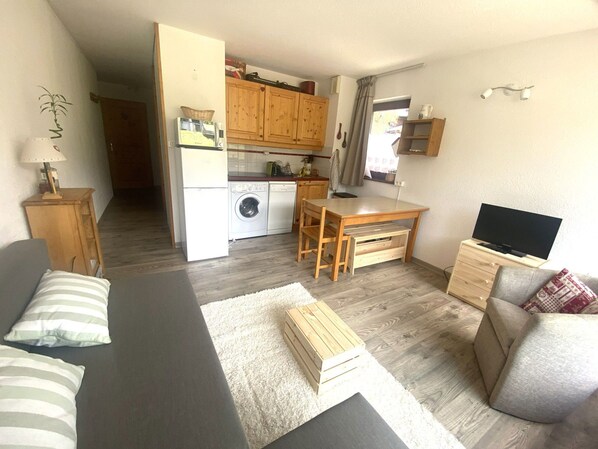 Ein kompakter Wohnbereich mit Küchenzeile, Essbereich und einer Sitzecke mit Sofa und Fernseher.