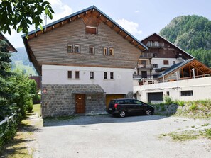 Ein zweistöckiges Gebäude mit Steinunterbau und Holzkonstruktion, vor dem ein Auto geparkt ist.