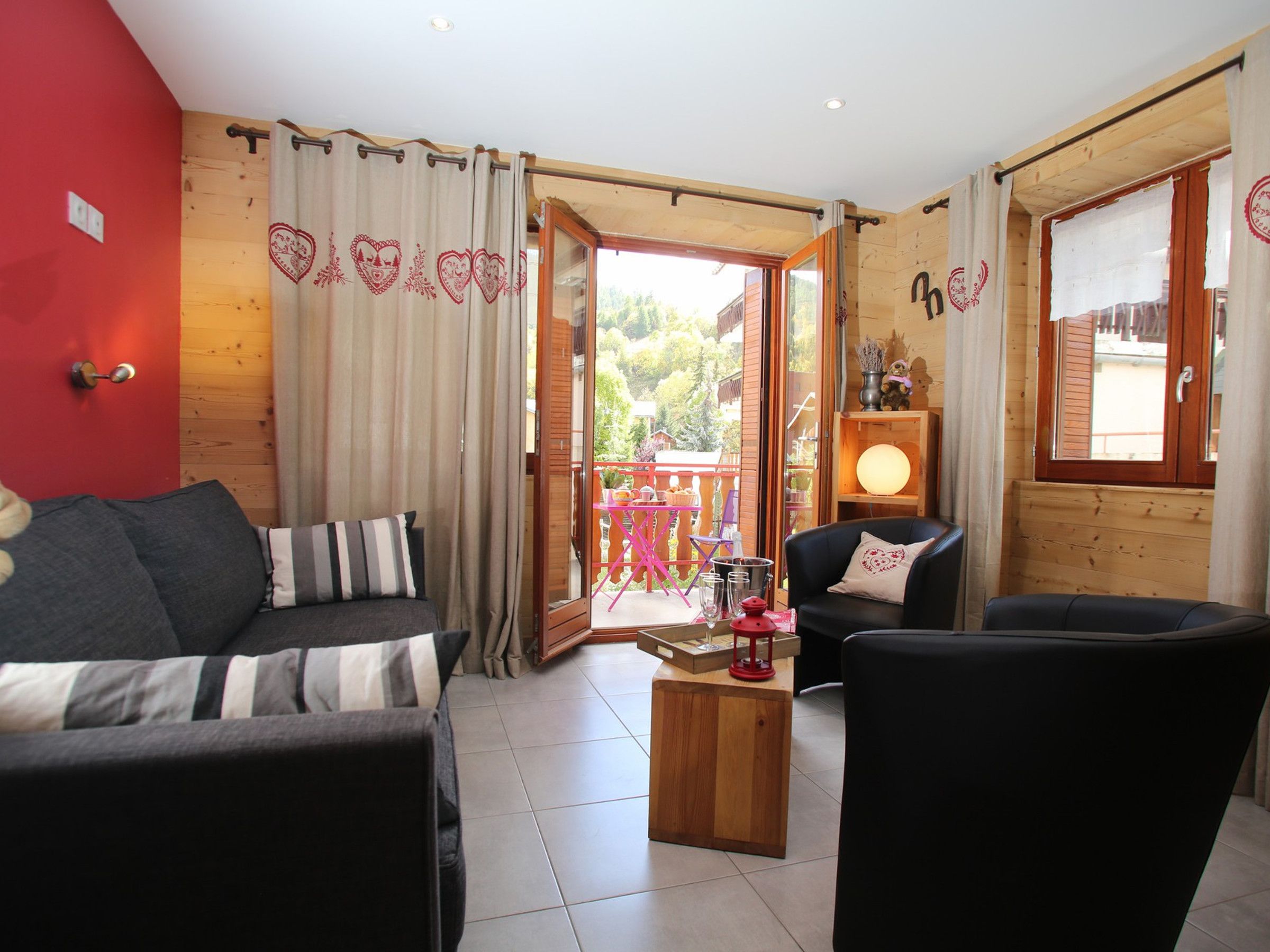 Un salon confortable avec un canapé, un fauteuil et une petite table basse. Une porte en bois donne accès à un balcon extérieur.