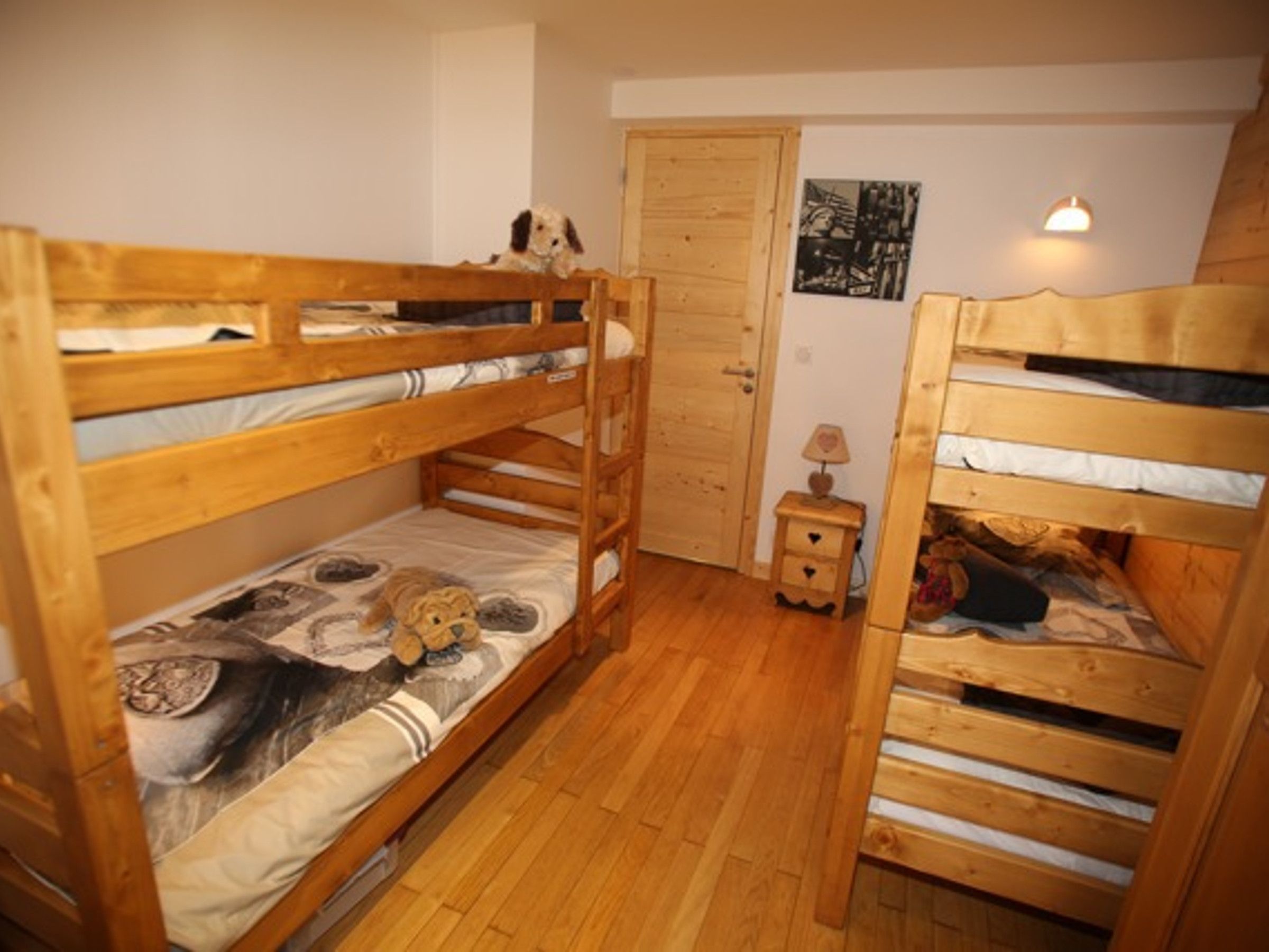 Une chambre avec deux lits superposés, une porte en bois, une petite table de chevet avec une lampe et un mur orné d’une photographie en noir et blanc.
