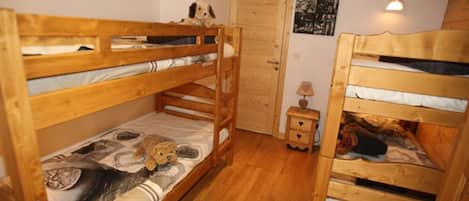 Une chambre avec deux lits superposés, une porte en bois, une petite table de chevet avec une lampe et un mur orné d’une photographie en noir et blanc.