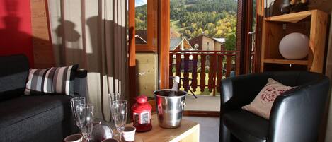 A cozy living room with a wooden coffee table, two sofas, and a balcony with a view of a forested hill.