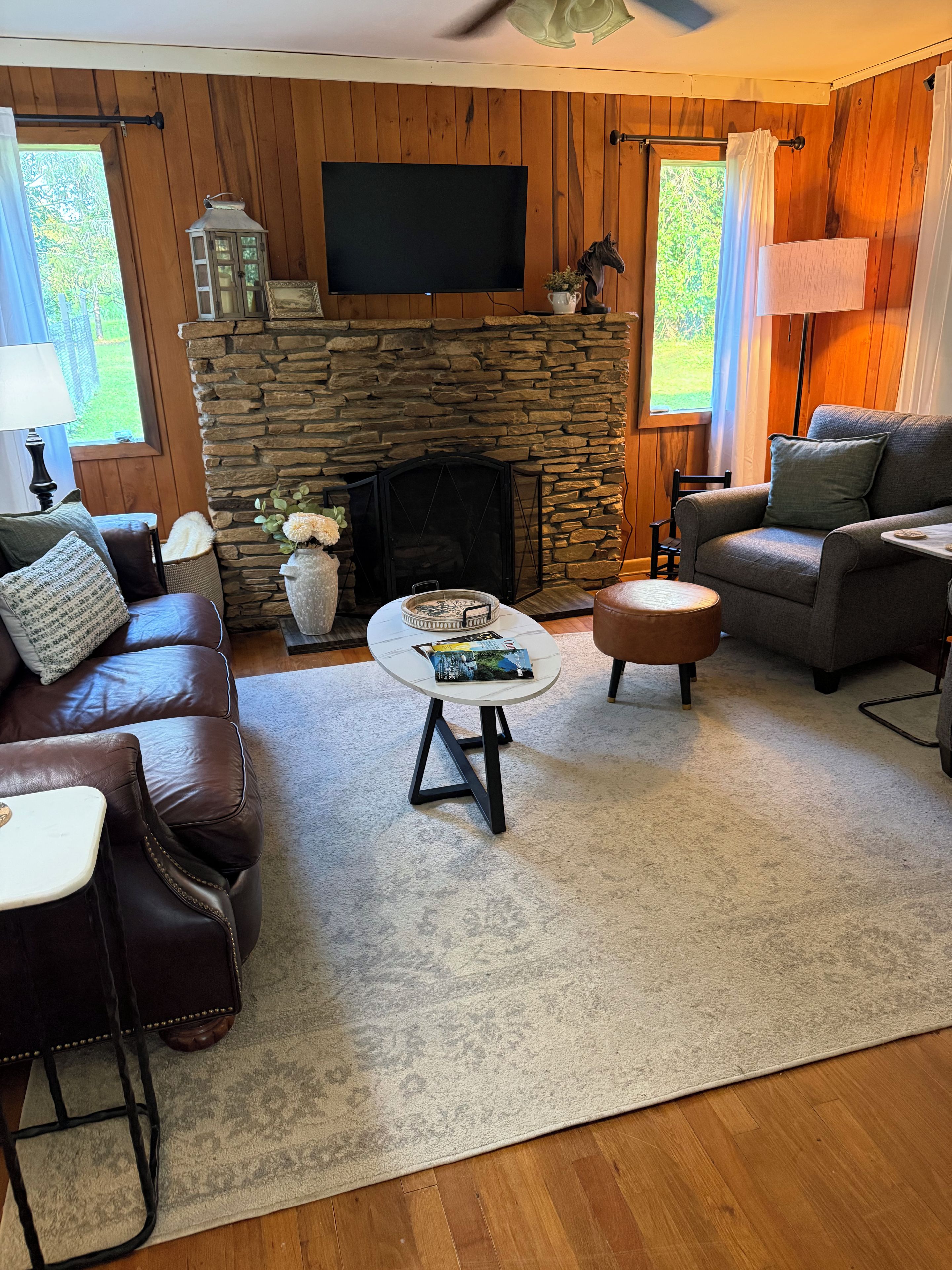 A cozy living room with a stone fireplace, leather furniture, and a flat-screen TV mounted above it.