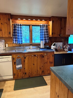 A kitchen with wooden cabinets, a stainless steel sink, and a window with blue curtains.