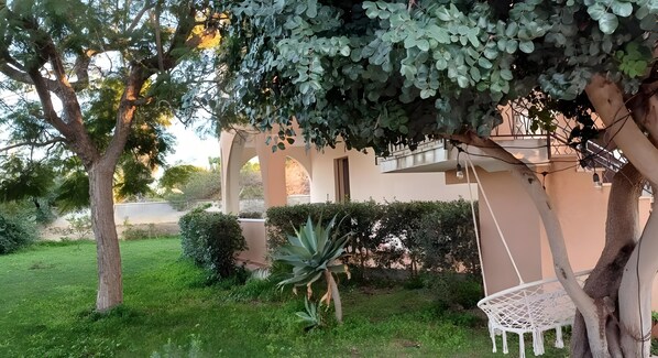 Un jardí amb una cadira blanca, un arbre i un edifici amb arcades.