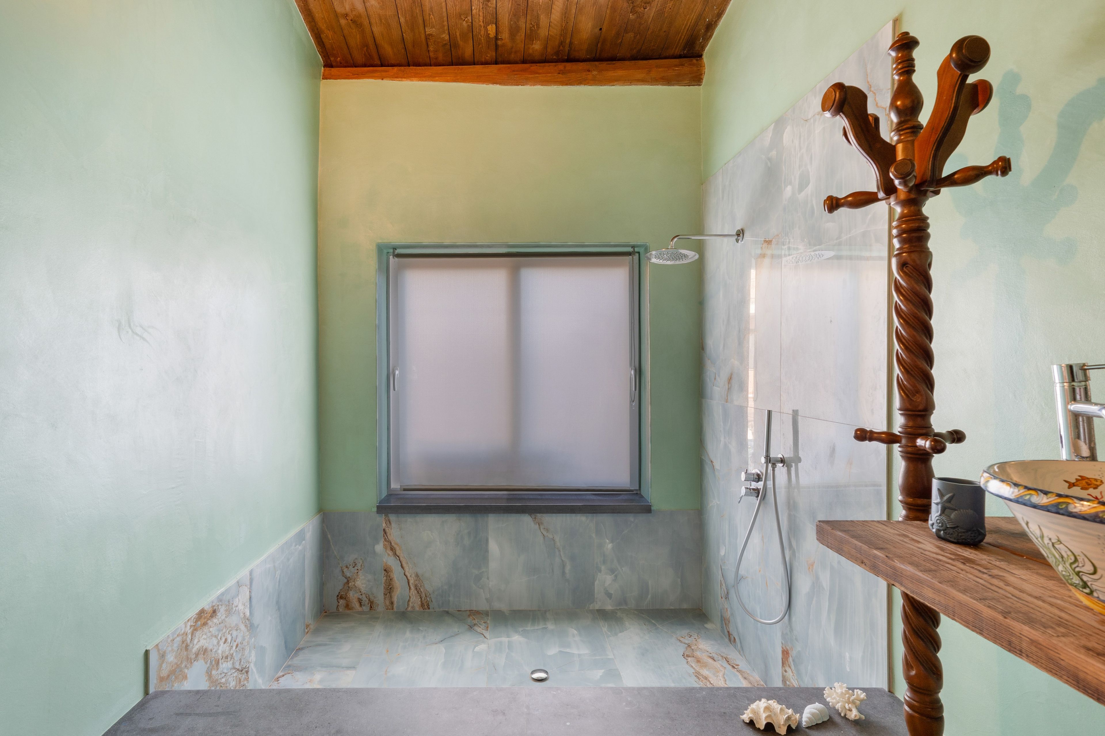 Ein Badezimmer mit Dusche, einer Holzwanne, einem Marmorboden und einem Holzwaschtisch mit Waschschüssel und Becher.
