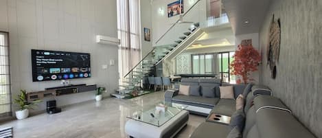 A spacious living area with a modern sofa set, a glass coffee table, and a flat-screen TV mounted on the wall.