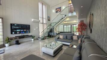 A spacious living area with a modern sofa set, a glass coffee table, and a flat-screen TV mounted on the wall.