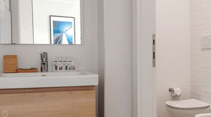 Ein modernes Badezimmer mit einem weißen Waschbecken, Spiegel und Toilette.