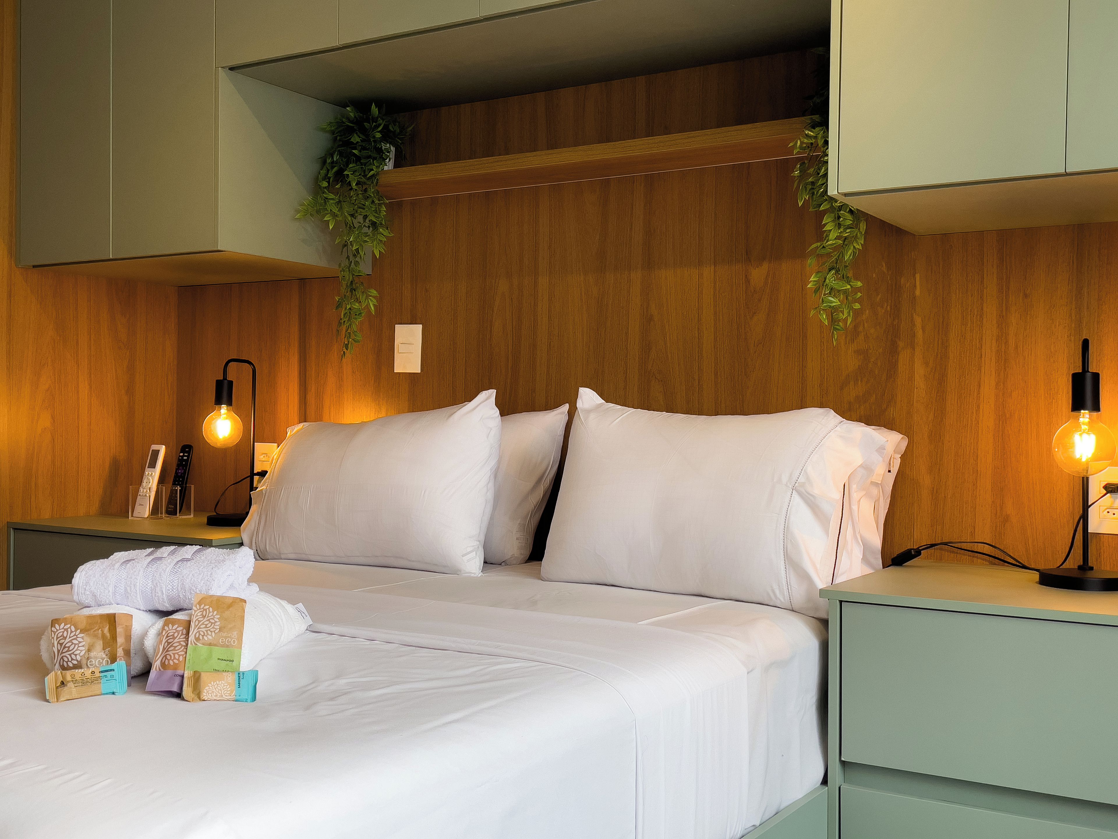 A neatly made bed with white linens, a bedside table with a lamp, and a nightstand with a remote control.
