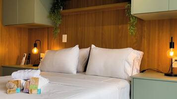 A neatly made bed with white linens, a bedside table with a lamp, and a nightstand with a remote control.