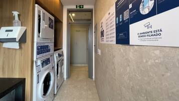 A hotel laundry room with multiple washing machines, a hand dryer, and informational posters on the wall.