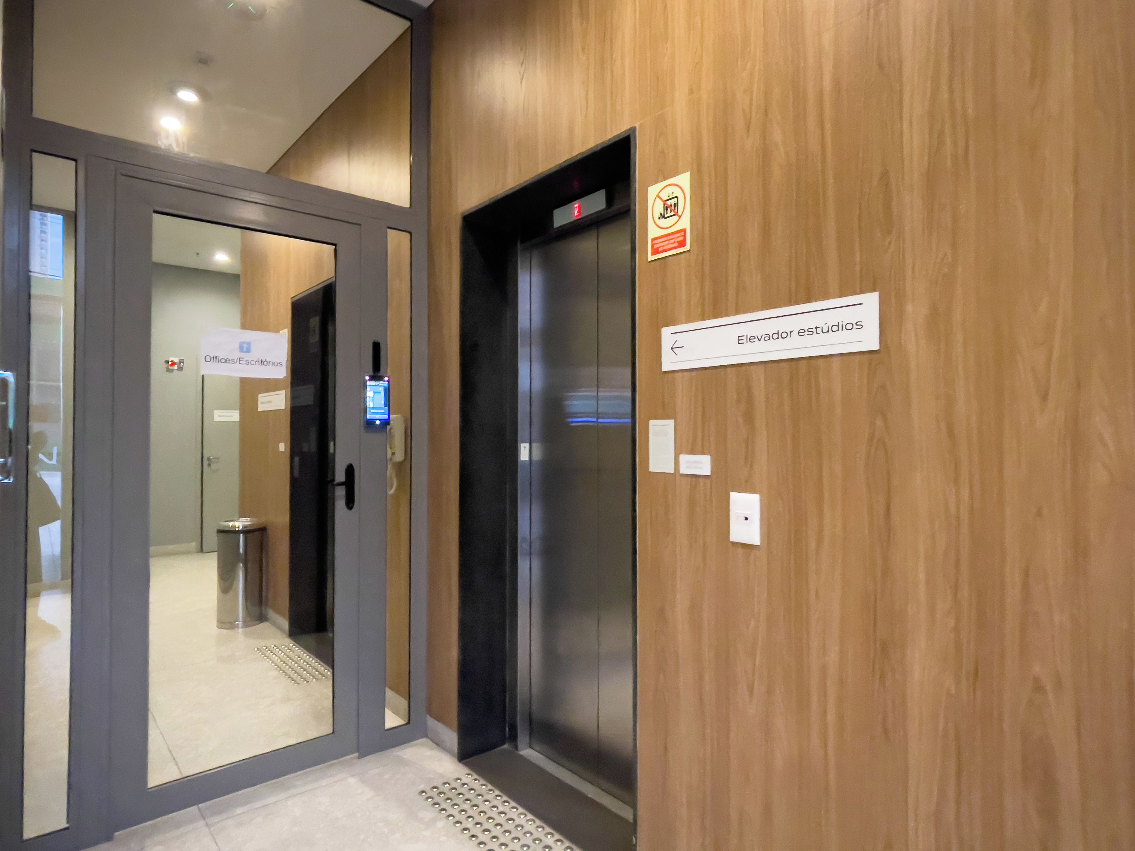 Un ascenseur doté d’un écran numérique, une signalétique indiquant l’emplacement des bureaux et du secrétariat, et un mur en bois.