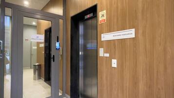 Un ascenseur doté d’un écran numérique, une signalétique indiquant l’emplacement des bureaux et du secrétariat, et un mur en bois.