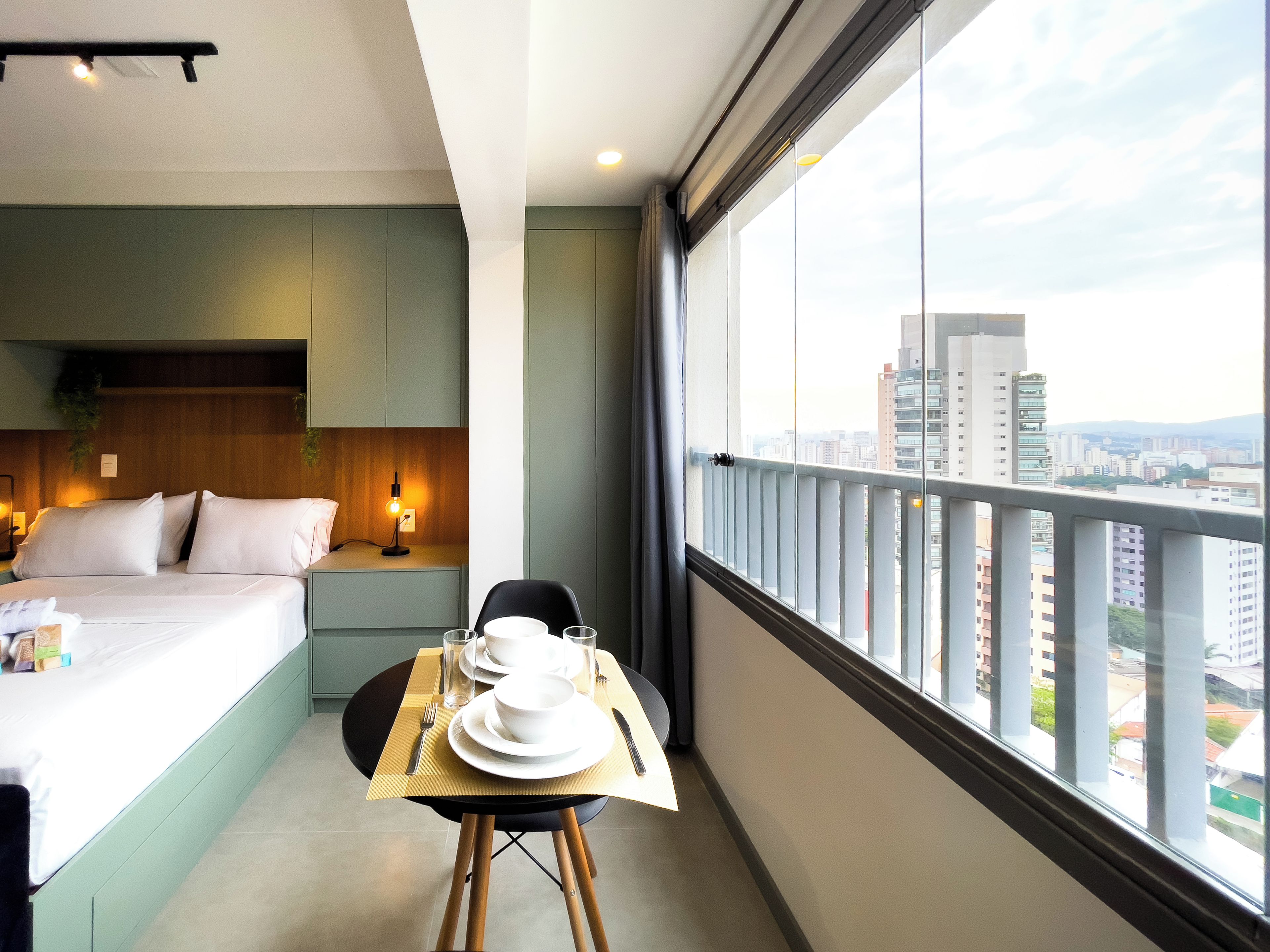 A hotel room with a bed, bedside table, and a dining area with a table set for two.