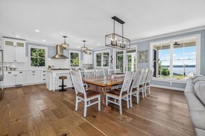 A spacious kitchen with a large dining table, white cabinetry, and a view of the outdoors. - Driftwood Daydream  Dog-friendly, lakefront house with beach access, dock, AC (St.Germain)