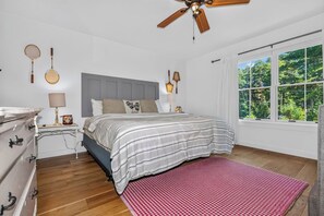 A bedroom with a bed, a nightstand, a dresser, a ceiling fan, and a window with a view of trees. - Driftwood Daydream  Dog-friendly, lakefront house with beach access, dock, AC (St.Germain)