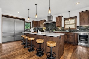 A modern kitchen with wooden cabinets, a stainless steel refrigerator, a large island with stools, and pendant lighting.