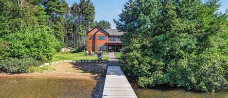 A wooden dock leading to a house surrounded by dense forest.