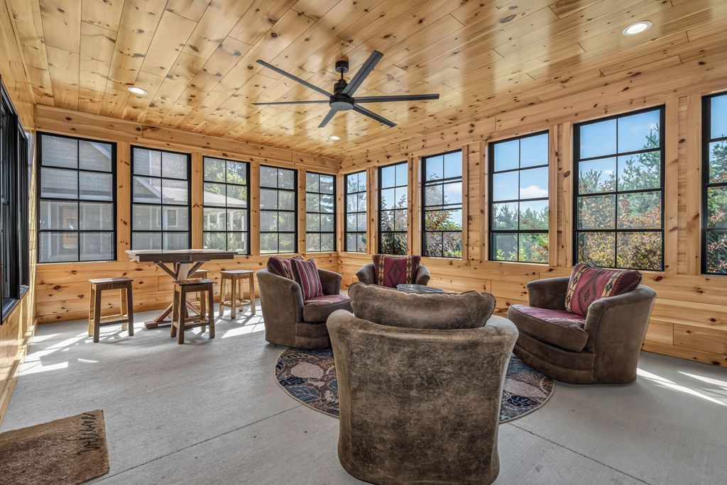 A spacious room with a high ceiling, wooden walls, large windows, and a ceiling fan.