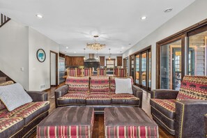 A spacious living room with a leather sofa set, a chandelier, and large windows.