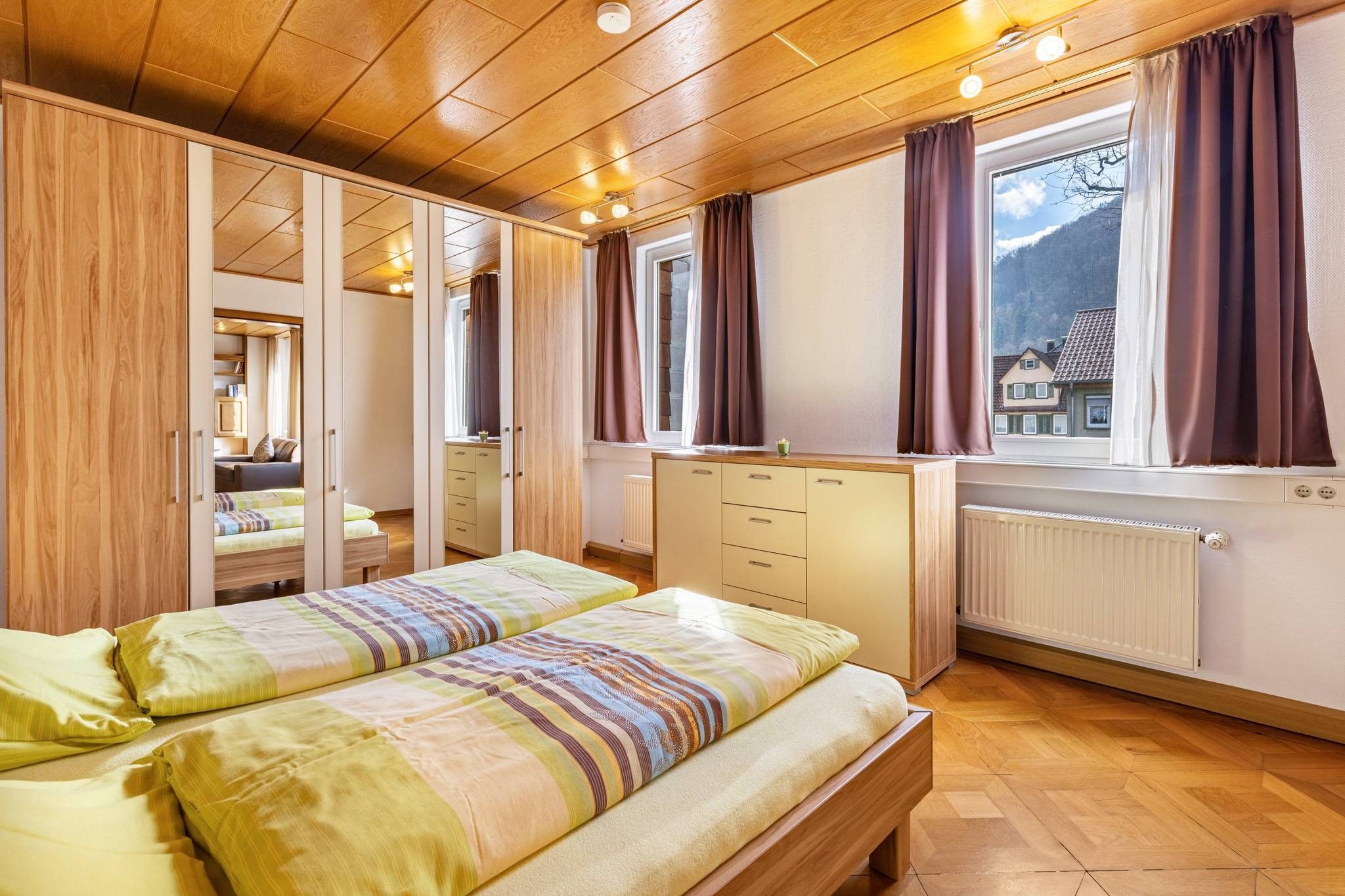 Ein Schlafzimmer mit zwei Betten, einem Schminktisch, einem Heizkörper und einem Fenster mit Vorhängen.