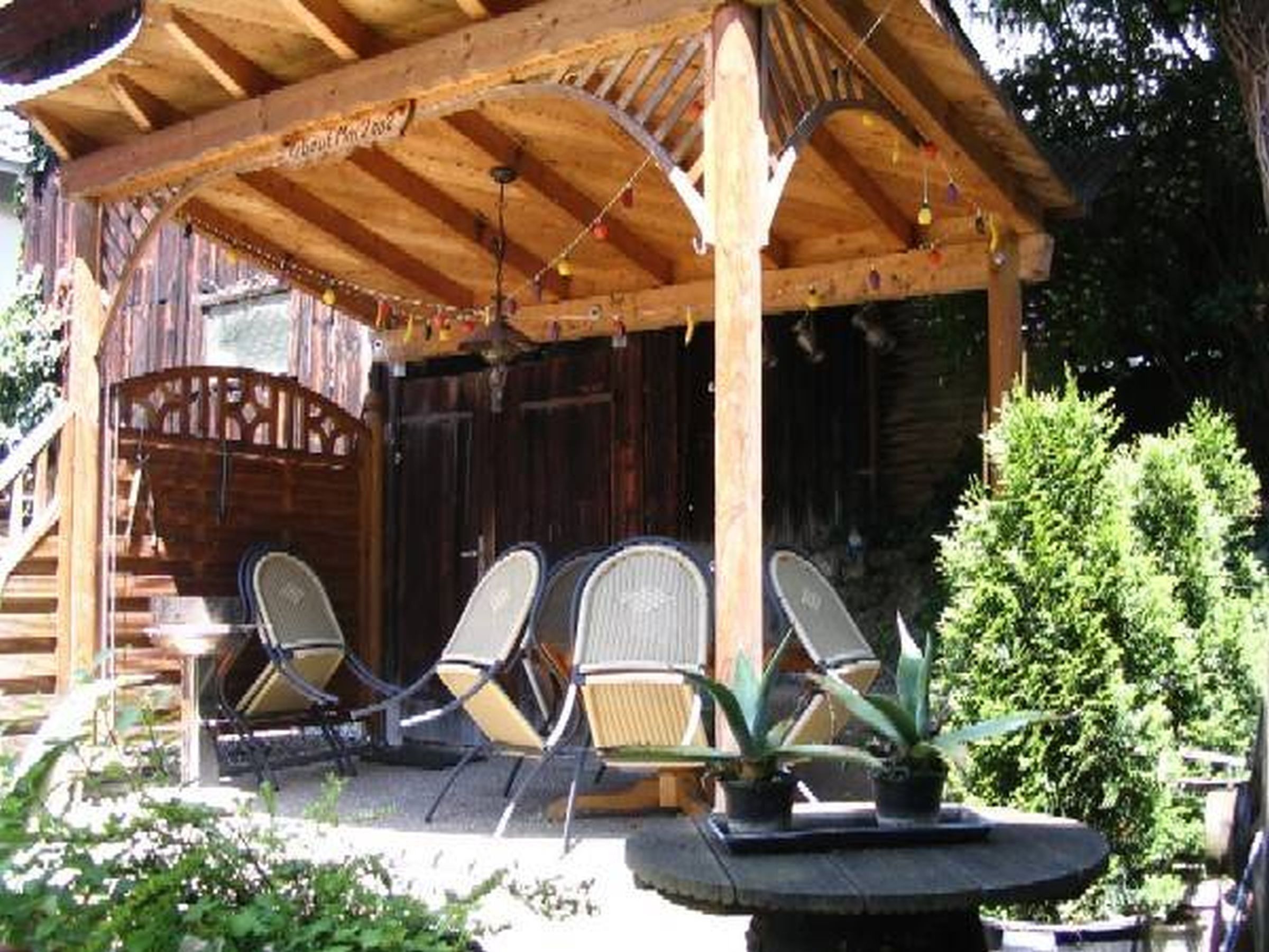 Ein hölzerner Pavillon mit überdachter Sitzgruppe, einer Treppe und einem kleinen Tisch mit Topfpflanzen.