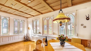 Un coin repas avec une table en bois, des chaises, un vase de fleurs, une bouteille de vin et un luminaire suspendu.