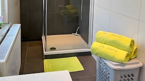 Une salle de bain moderne avec une douche à parois de verre, une baignoire blanche et un panier à linge contenant des serviettes jaunes.