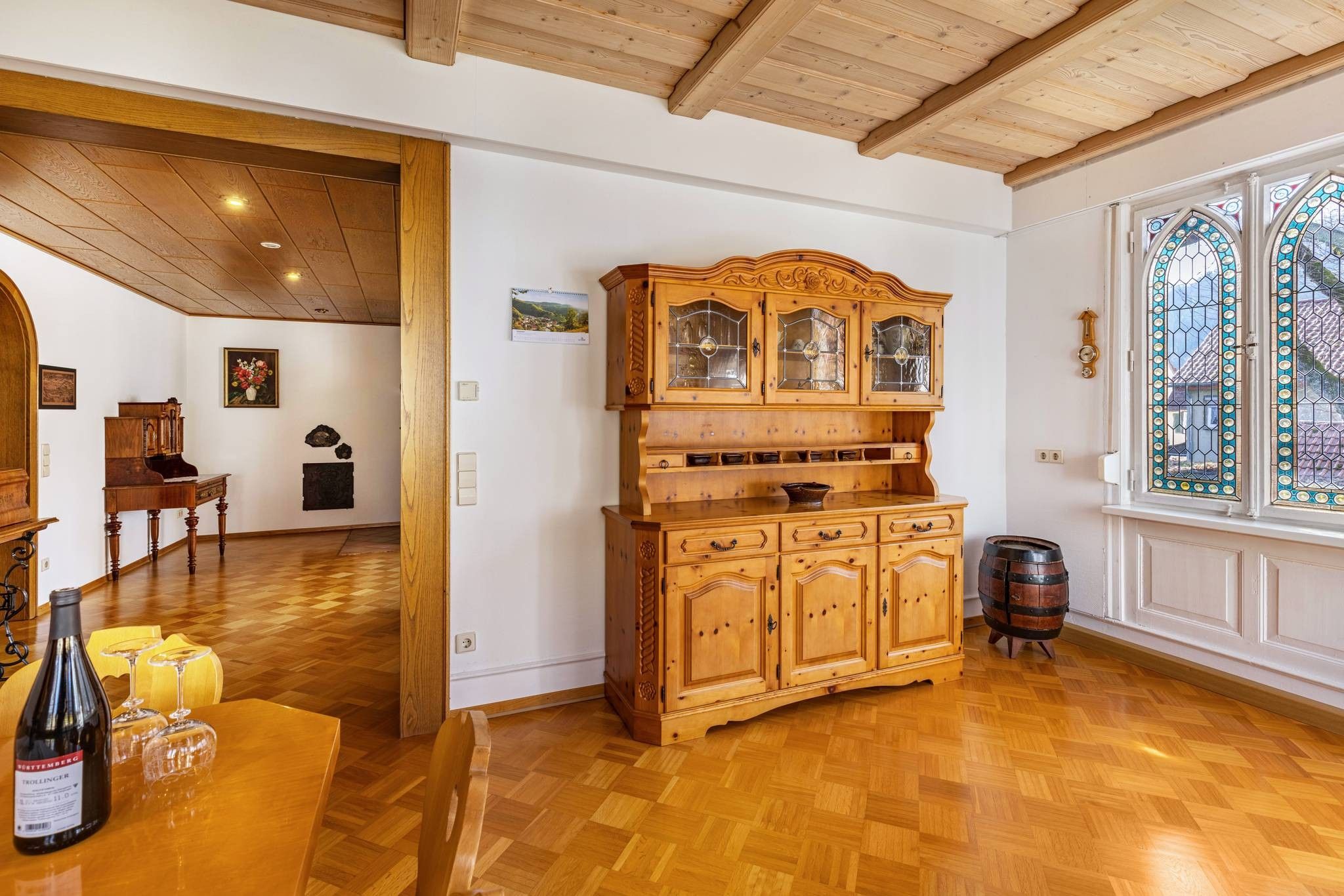 Ein Holzkabinett mit Glastüren, ein Holztisch mit Weinflaschen und Gläsern sowie ein Holzfass.