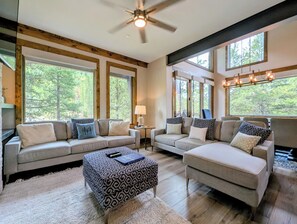 A spacious living room with two sofas, a coffee table, and a ceiling fan. Large windows provide views of the outdoors. - NEW | Updated | Forest Views | Free Shuttle (Keystone)