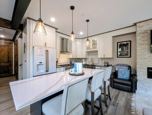 Une cuisine moderne avec des meubles blancs, un plan de travail en marbre, des luminaires suspendus et un coin bar avec des tabourets.