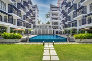 Ein modernes Hotel mit einem zentral gelegenen Schwimmbecken, umgeben von üppiger Vegetation und einer gepflegten Rasenfläche.