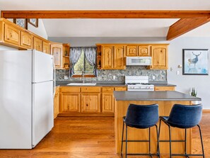 A kitchen with wooden cabinets, a white refrigerator, a stove, and a window with checkered curtains. - Emberwood | Hot Tub, 2 Fireplaces, Sleeps 9 (Heber)
