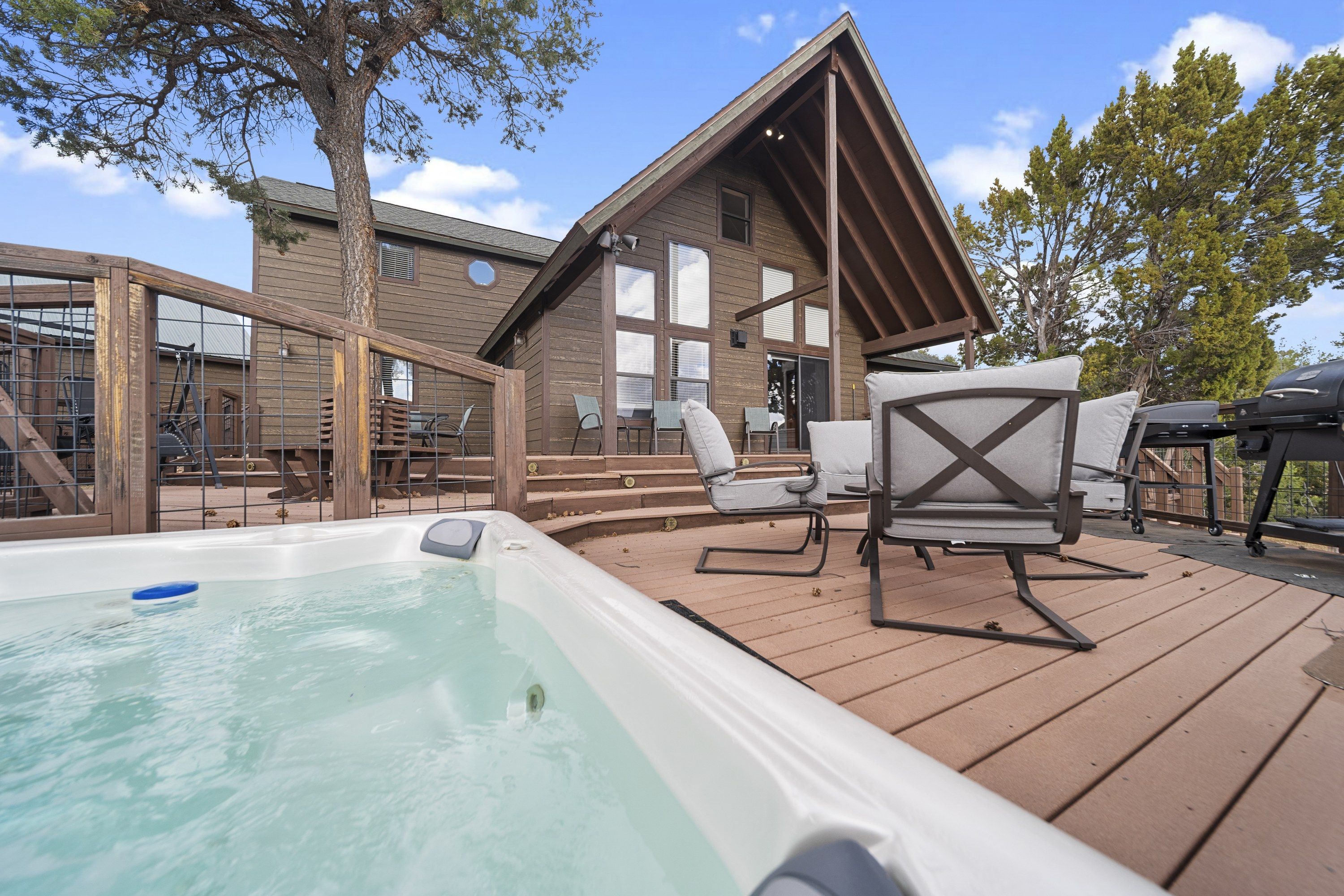 A wooden deck with a hot tub, outdoor seating, and a building with large windows.