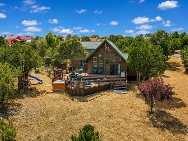 A wooden cabin with a deck, surrounded by trees and a playground. - Emberwood | Hot Tub, 2 Fireplaces, Sleeps 9 (Heber)